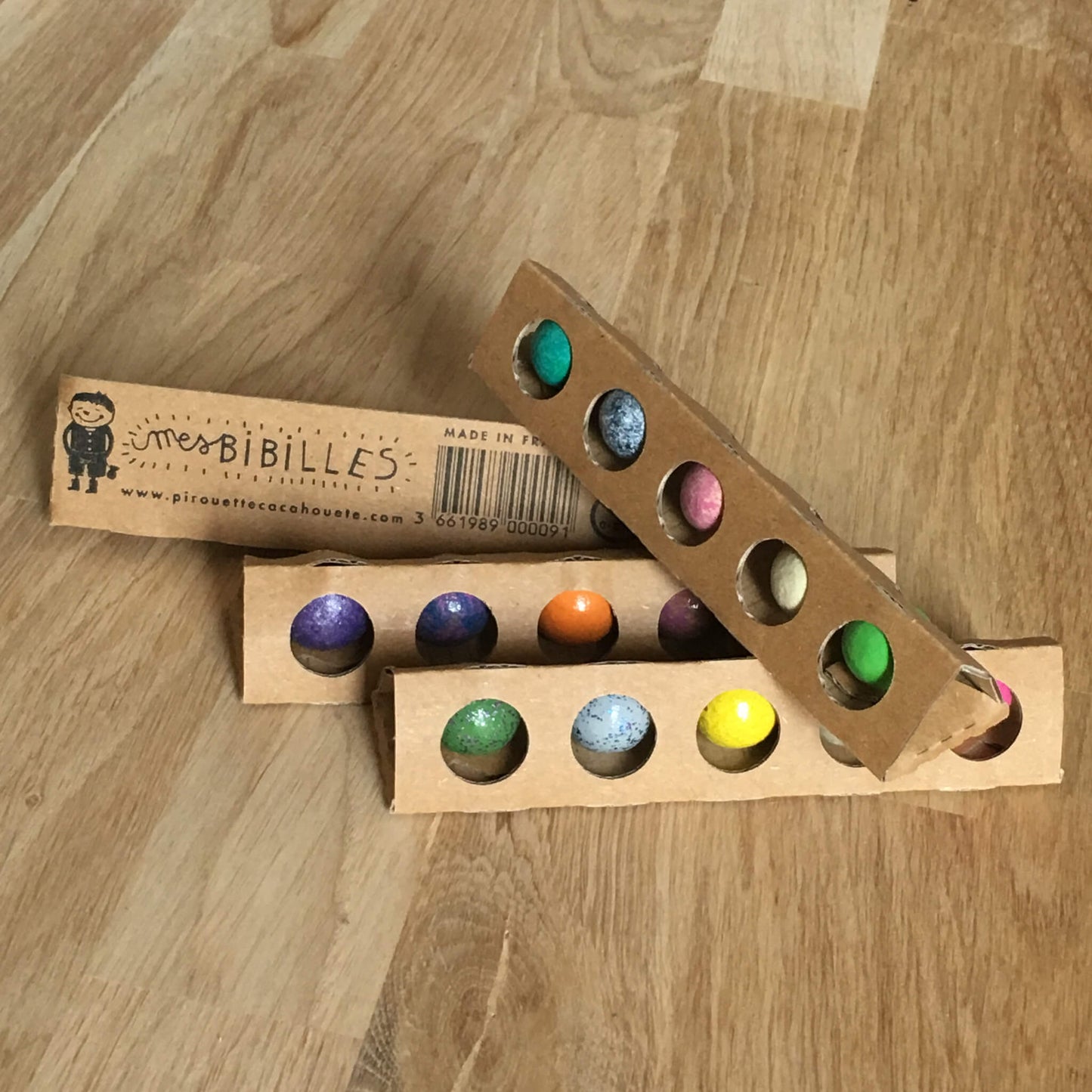4 tubes en carton beige avec 5 billes multicolores en terre posées sur un parquet