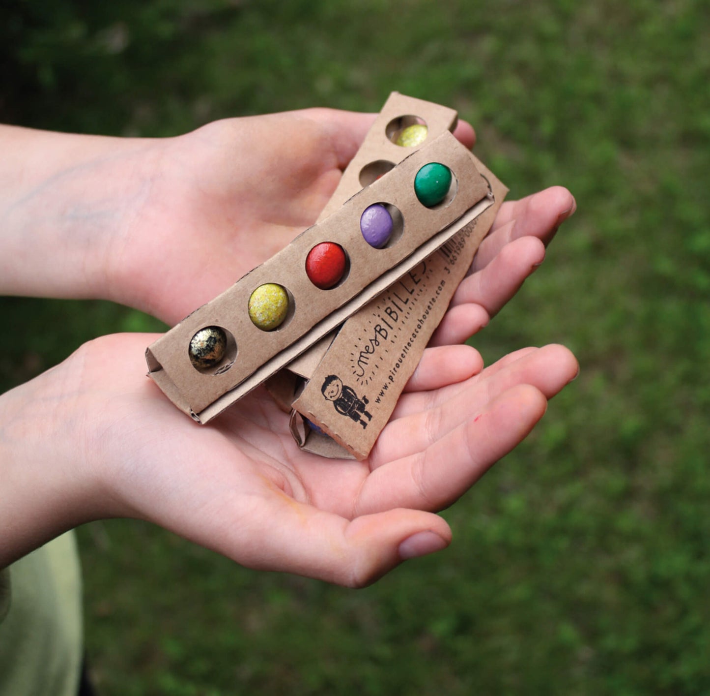 mains présentant 3 tubes en carton beige avec 5 billes multicolores en terre