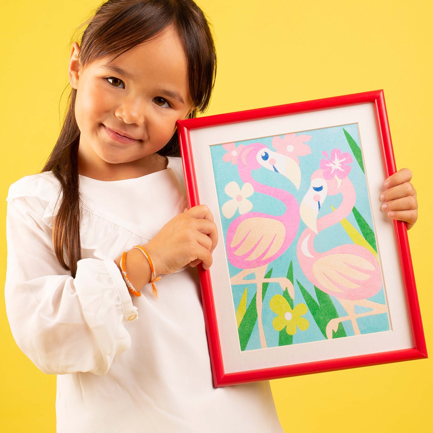 petite fille de 4 ans tenant un cadre rouge dans lequel se trouve un tableau sablimage représentant des flamants roses