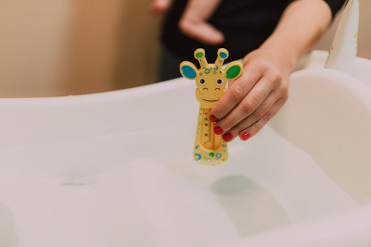 main de maman vérifiant avec un thermometre girafe la temperature de l'eau pour le bain enveloppé de bebe