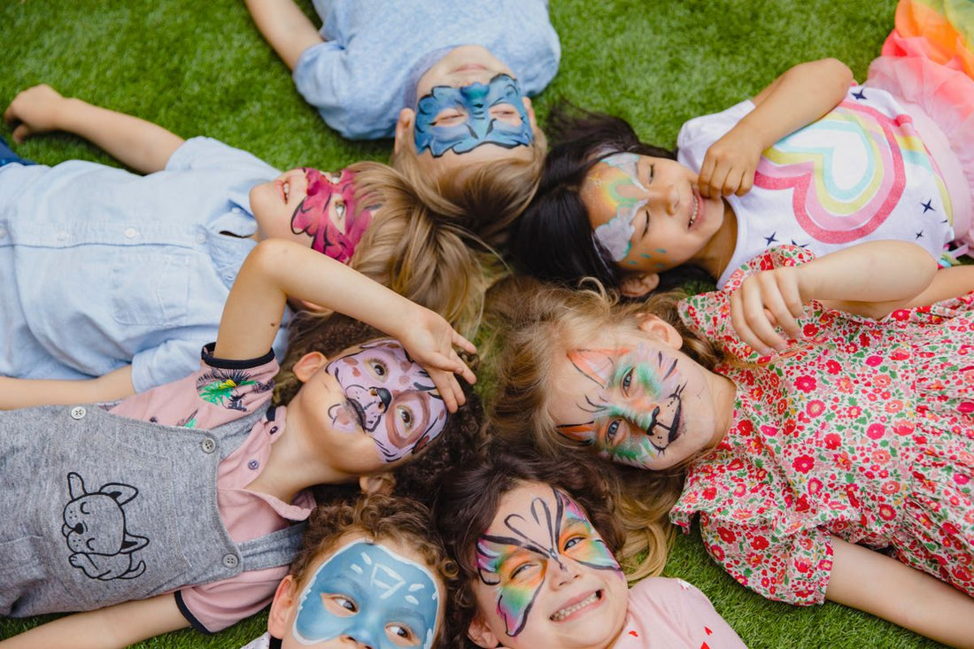 7 enfants couchés dans l'herbe avec un maquillage d'anniversaire, une super idée d'activité pour un anniversaire de 5 ans