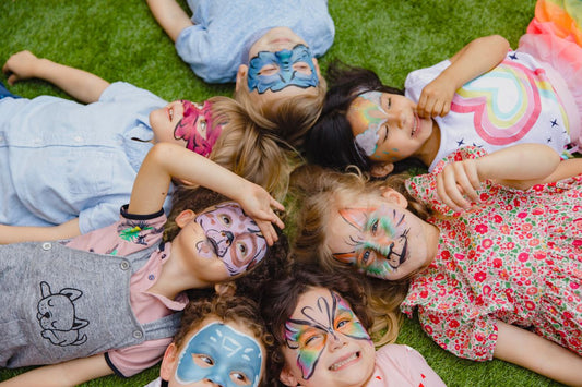 7 enfants couchés dans l'herbe avec un maquillage d'anniversaire, une super idée d'activité pour un anniversaire de 5 ans