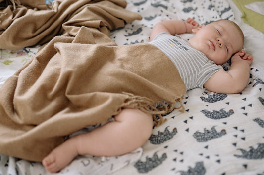 bébé endormi sur le dos sur un lange à motifs éléphants avec une couverture beige posée sur lui