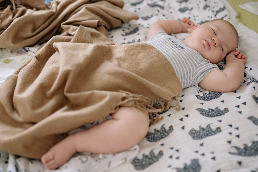 bébé endormi sur le dos sur un lange à motifs éléphants avec une couverture beige posée sur lui