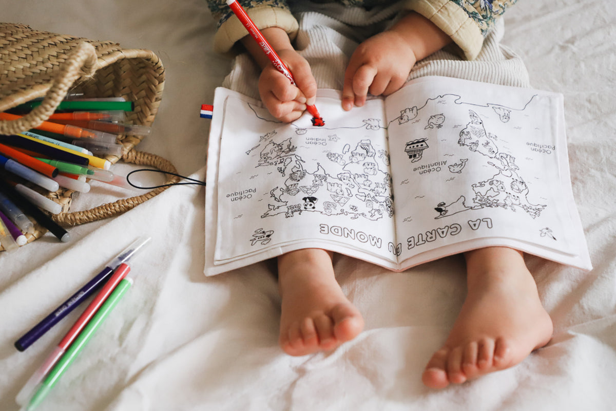 enfant de 3 ans qui colorie un cahier de coloriage lavable mappemonde posé sur ses genoux