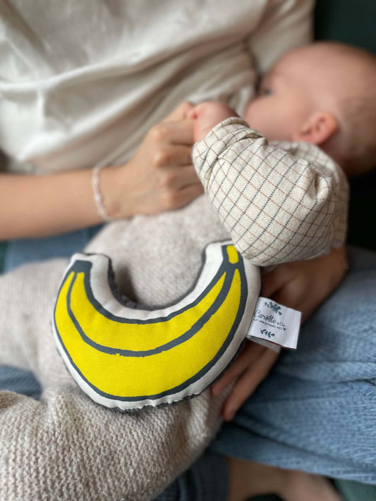 bébé dans les bras de sa maman avec un hochet en coton bio en forme de banane posé sur son ventre