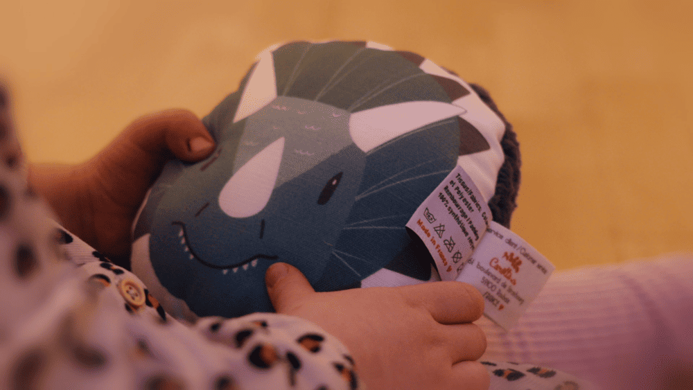 enfant 2 ans tenant un coussin musical à tête de dinosaire