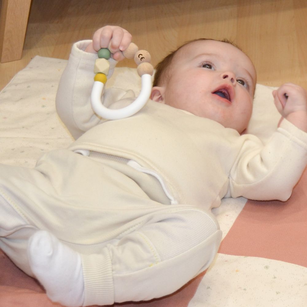 bébé de 4 mois allongé sur le dos et tenant dans sa main un jouet de dentition certifié CE sans danger pour les tout-petits