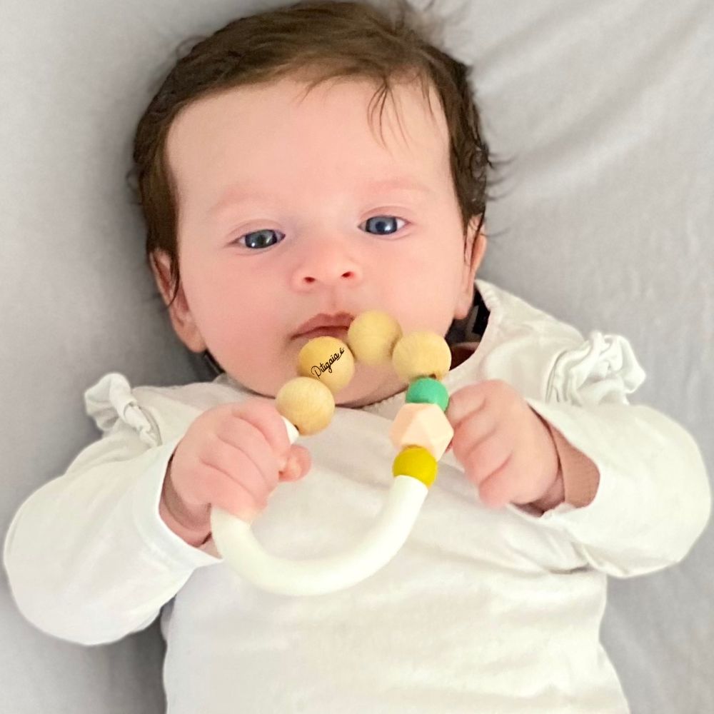 bébé de 6 mois allongé tenant dans sa main un jouet de dentition bi-matière certifié CE