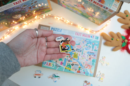 main tenant une pièce du puzzle en bois pour enfants dès 6 ans représentant la carte de paris et ses monuments