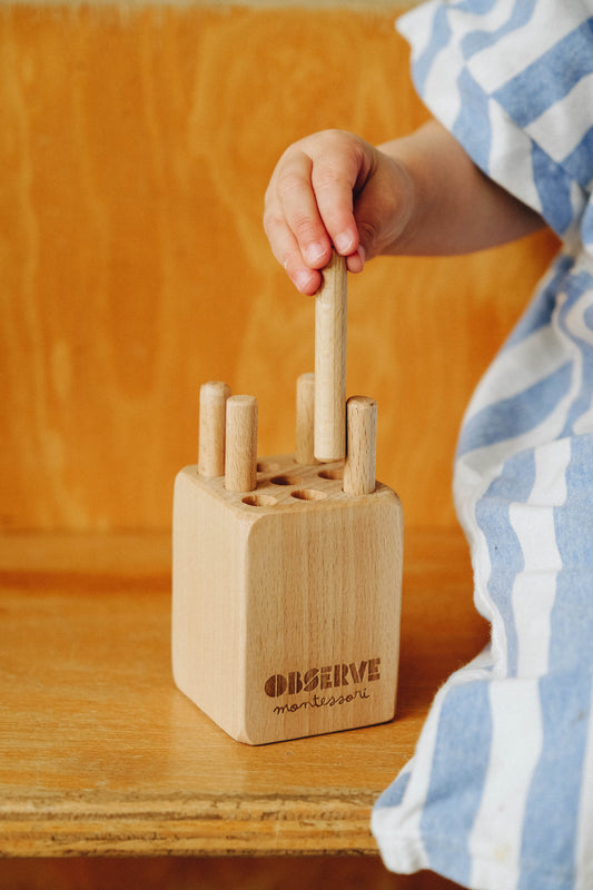 enfant mettant un tourillon dans le socle  en bois du jeu montessori 18 mois