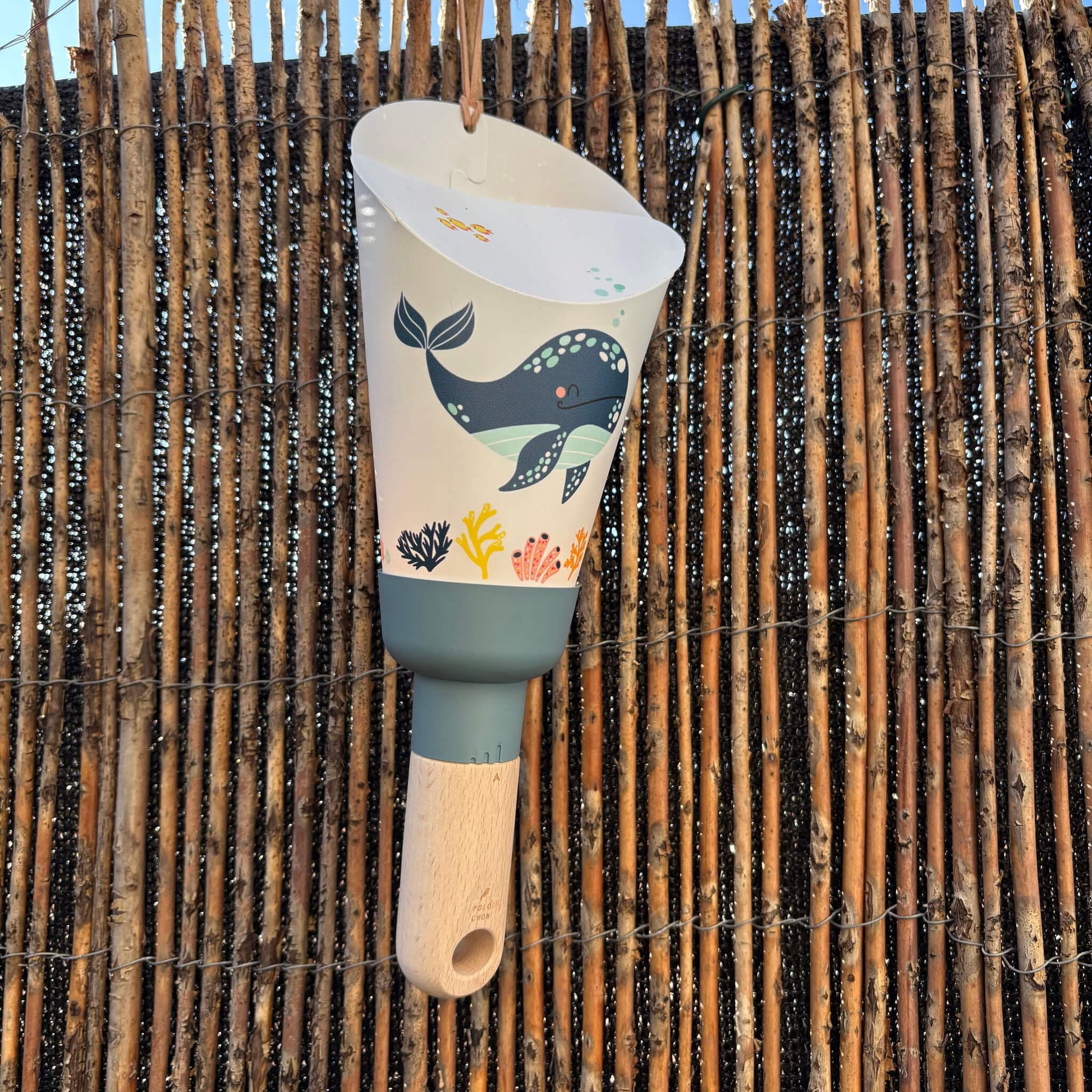 lampe veilleuse pour enfant maison polochon au design baleine, suspendue devant un panneau en rotin